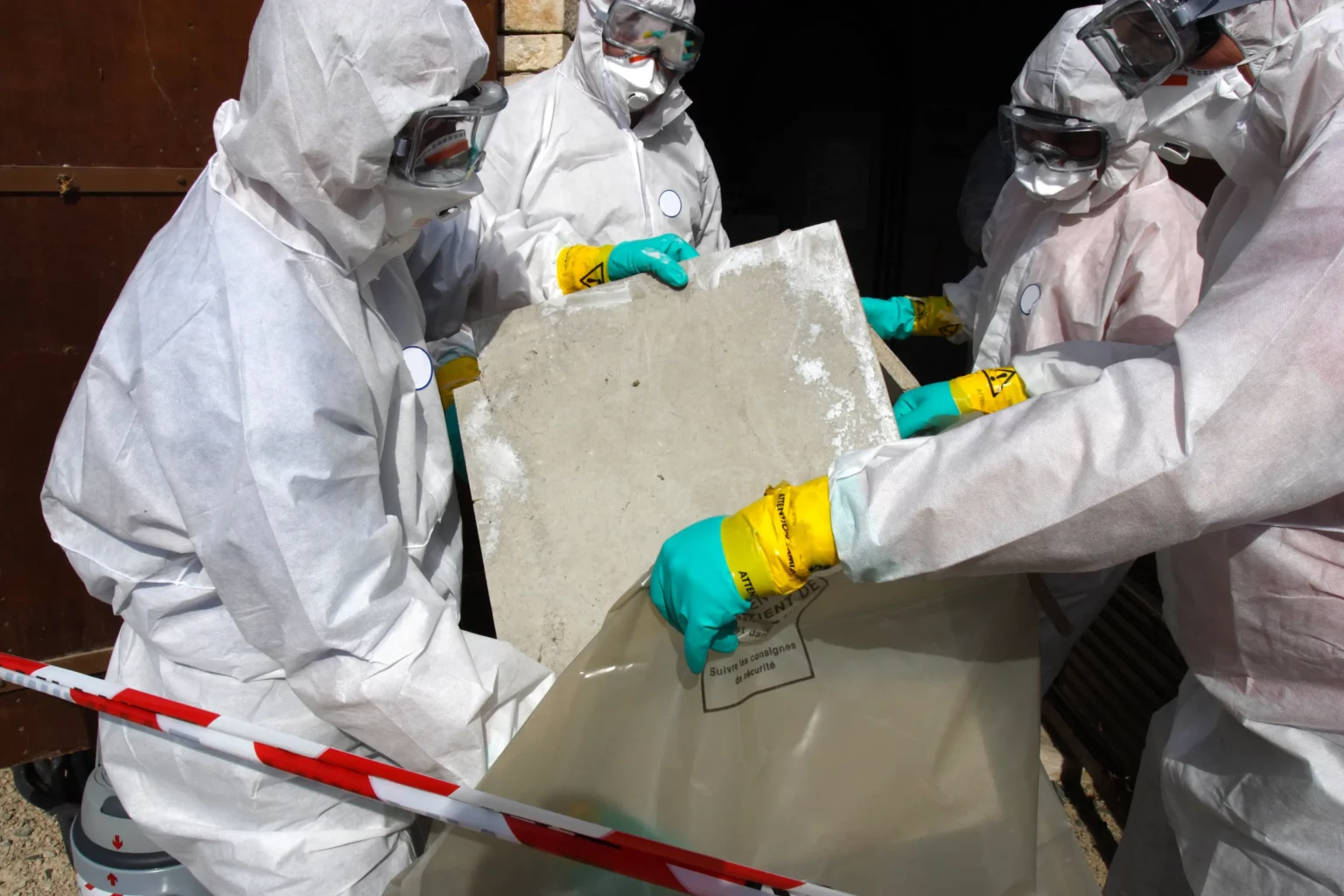 Asbestos removal contractors in PPE bagging an asbestos sheet for disposal