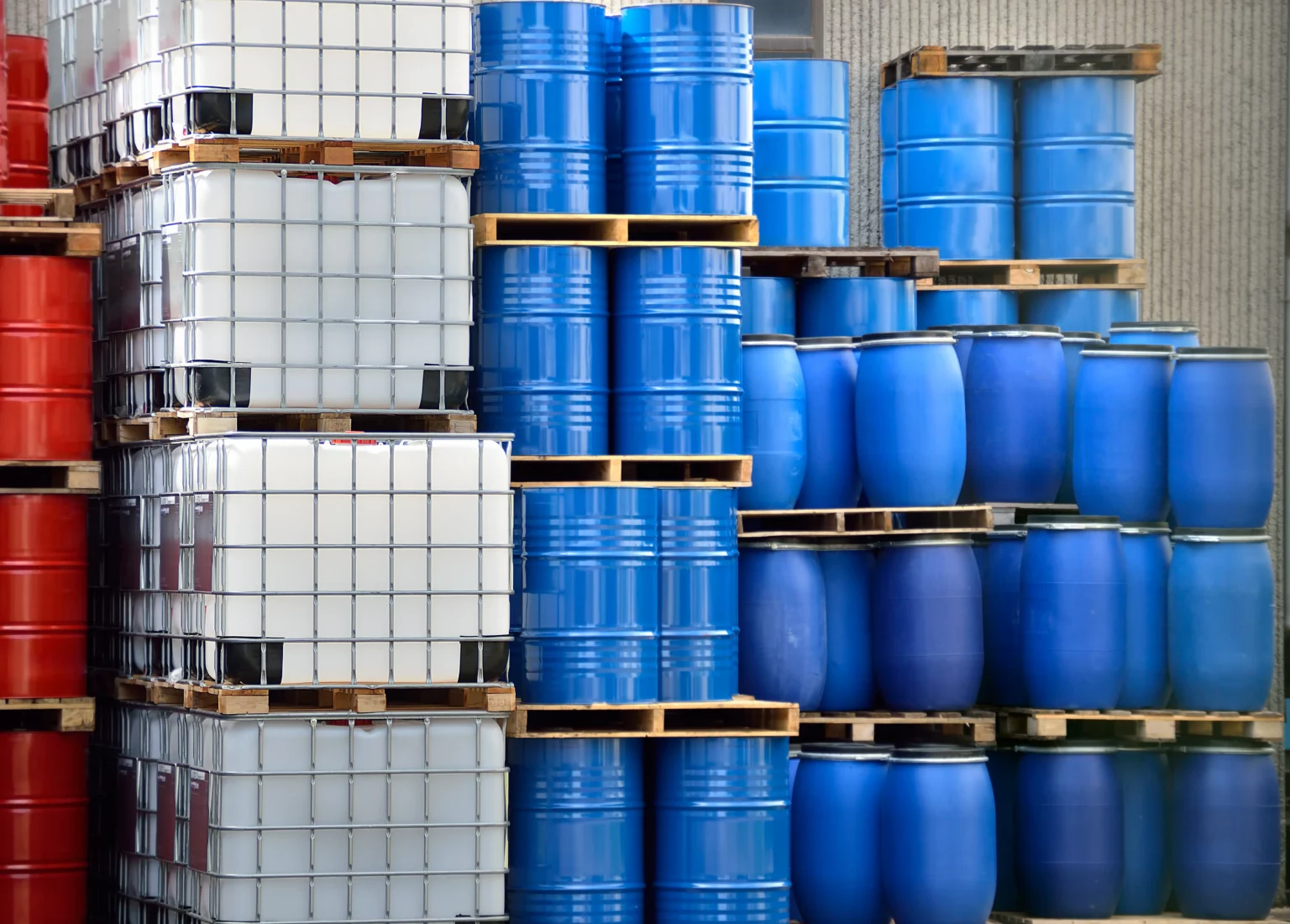 Stacked blue plastic barrels and white intermediate bulk containers (IBCs) at a chemical manufacturing facility